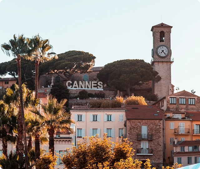 Vue pittoresque de Cannes sur la Côte d'Azur, avec des palmiers, une architecture méditerranéenne, des bâtiments en hauteur et une horloge historique.