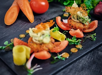 Plat créatif de haute cuisine avec des légumes et des garnitures délicates servi sur une assiette sombre.