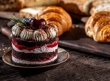 Gâteau au chocolat et aux cerises en couches servi avec des croissants fraîchement cuits sur une table rustique.