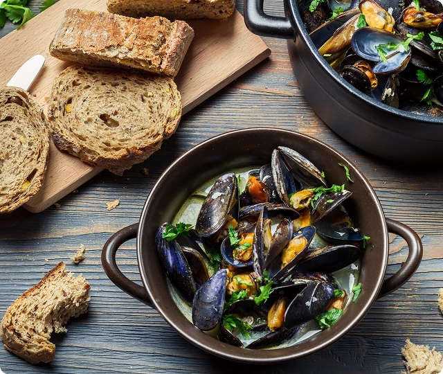 Moules fraîches servies dans une sauce riche avec du pain rustique et des herbes.