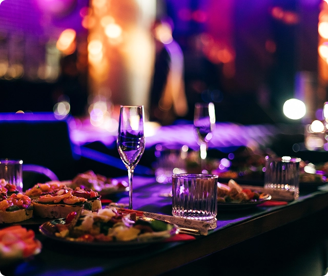 Table de restaurant élégante avec des amuse-bouches et des boissons illuminées par un éclairage violet atmosphérique.