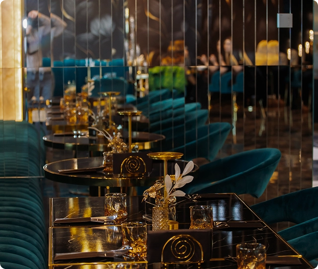 Intérieur de restaurant élégant avec des sièges en velours vert foncé, des tables brillantes, un éclairage doré chaleureux et une décoration contemporaine raffinée.